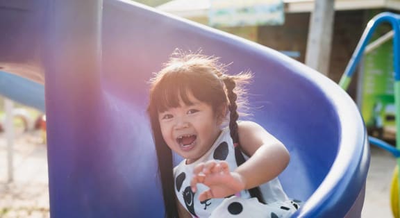 a little girl smiling as she slides down a playground slide