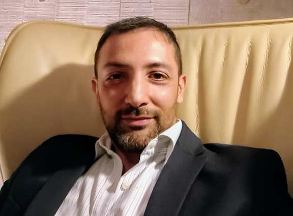 A man with a beard is wearing a black suit and a white shirt.