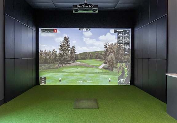 A room with a Deveraux Apartment Communities sign on the wall and a golf simulator at Podium Apartments, Calgary, AB