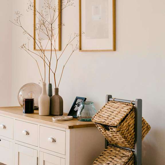 A white dresser with art above decorative accessories and a vase with branches on top of it.