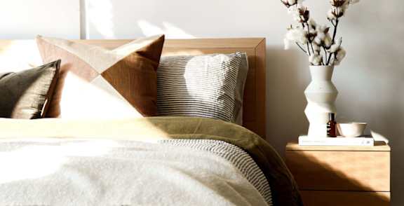 A bed with a white pillow and a brown pillow with a tan pillow case and a white blanket.