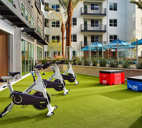 A row of stationary bikes are lined up on a green lawn in front of a white building.