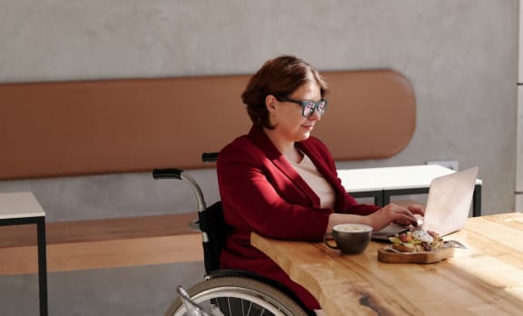 a woman in a wheelchair sitting at a table with a laptop