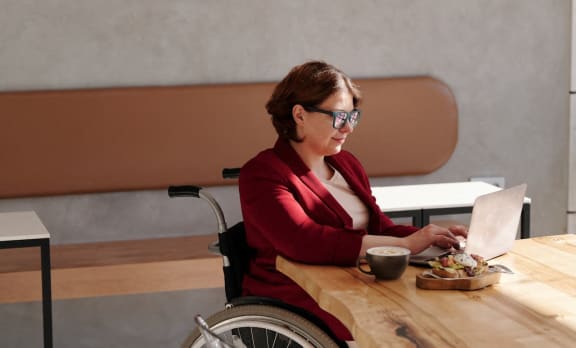 a woman in a wheelchair sitting at a table with a laptop