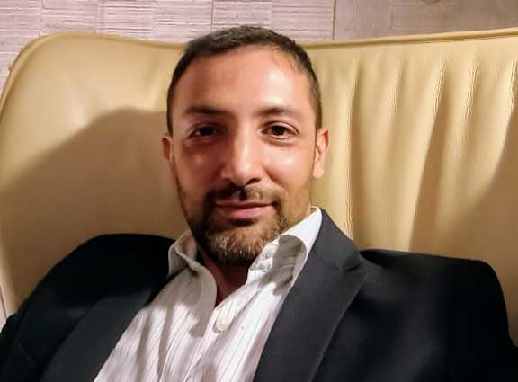 A man with a beard is wearing a black suit and a white shirt.
