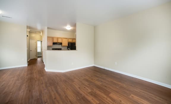 an empty living room with wood flooring and a kitchen