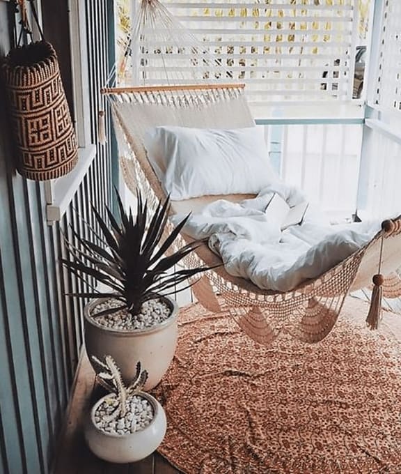 a hammock on a balcony with pillows and a plant