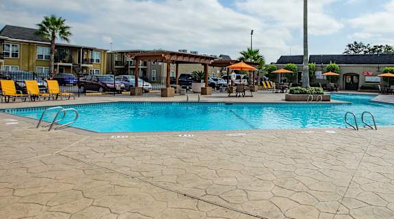 A large outdoor swimming pool surrounded by palm trees and lounge chairs at Willow Creek Apartments, Houston