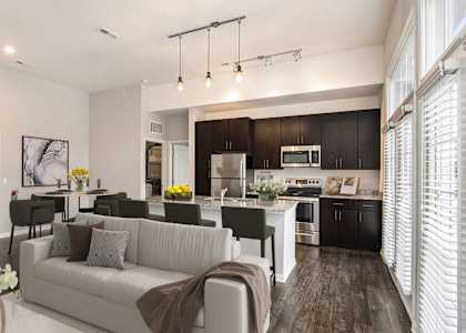 A modern living room with a grey sofa and a kitchen in the background.