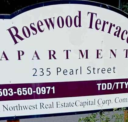 A sign for Rosewood Terrace Apartments is displayed in front of a flower bed.