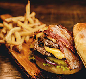 a cheeseburger with bacon and a side of french fries on a wooden board