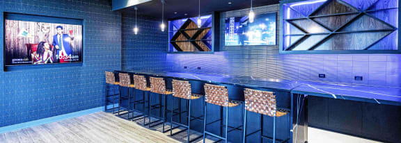 A contemporary bar at 3THIRTY3 Apartments with blue accent lighting, high stools, and multiple TVs, creating a vibrant social atmosphere.