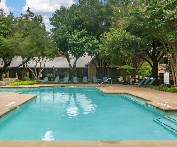 a resort style pool with chaise lounge chairs and trees