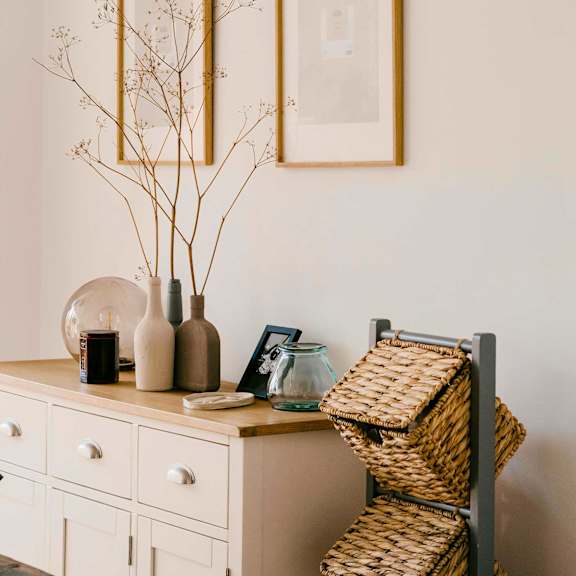 Entry decor of a white dresser holding pottery and a picture frame against a beige wall
