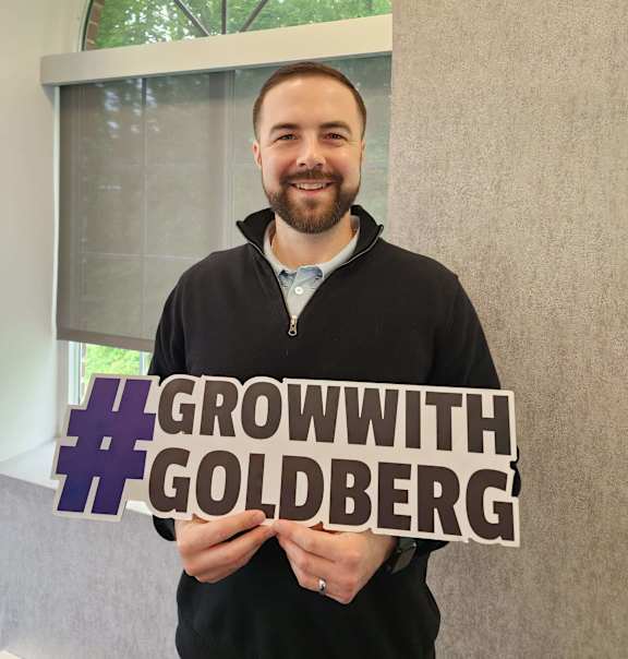 A man holding a sign that says #GROWWITH #GOLDBERG.