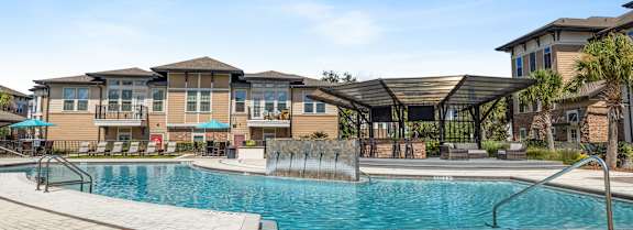 A large swimming pool in front of a building with a covered patio area.