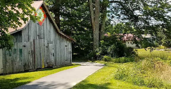 A wooden barn with a red and white sign on the door is situated next to a tree and a grassy path.