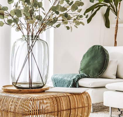 A living room with a white couch, a wicker table, and a vase with greenery.
