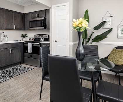 a dining area with a table and chairs and a kitchen in the background
