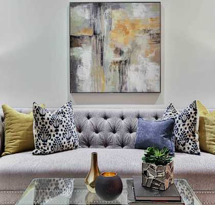Plush couch with throw pillows, coffee table, trinkets, lamps, and large wall art above