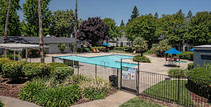 swimming pool and spa area with lounge chairs, umbrellas, and tables at Woodbridge Apartments, Sacramento, California 95833