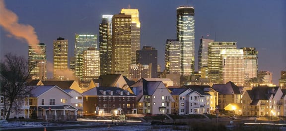 A nighttime photo of Hertiage Park apartments and townhomes with the skyline of Minneapolis in the background 
