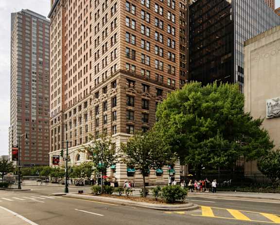 A large brown building with many windows sits in the middle of a city street at One West, New York, New York.