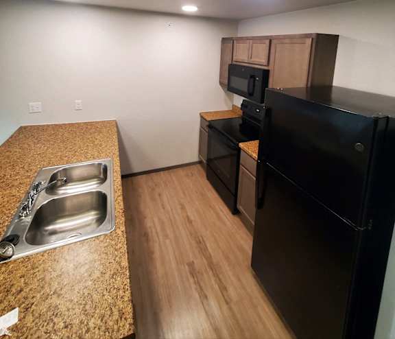 A kitchen with a black fridge and a granite counter top.