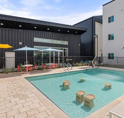 a swimming pool with tables and umbrellas in front of a building at SECOND AVE COMMONS | BRAND-NEW, Mesa, AZ, 85210