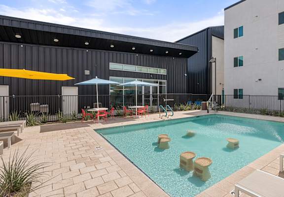 a swimming pool with tables and umbrellas in front of a building at SECOND AVE COMMONS | BRAND-NEW, Mesa, AZ, 85210