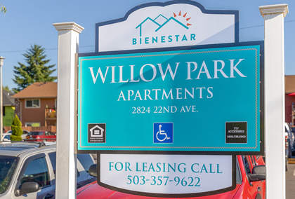 A sign for Willow Park Apartments stands in front of a parking lot.