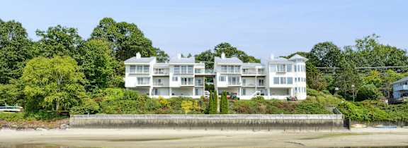 A large white building sits on a beach with trees in the background.