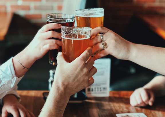 A group of people toasting with beer glasses at a bar.