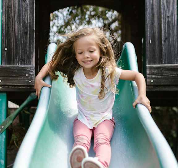 A young girl sliding down a green slide.