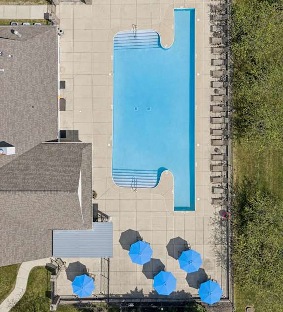 A large swimming pool surrounded by a concrete patio and blue umbrellas.