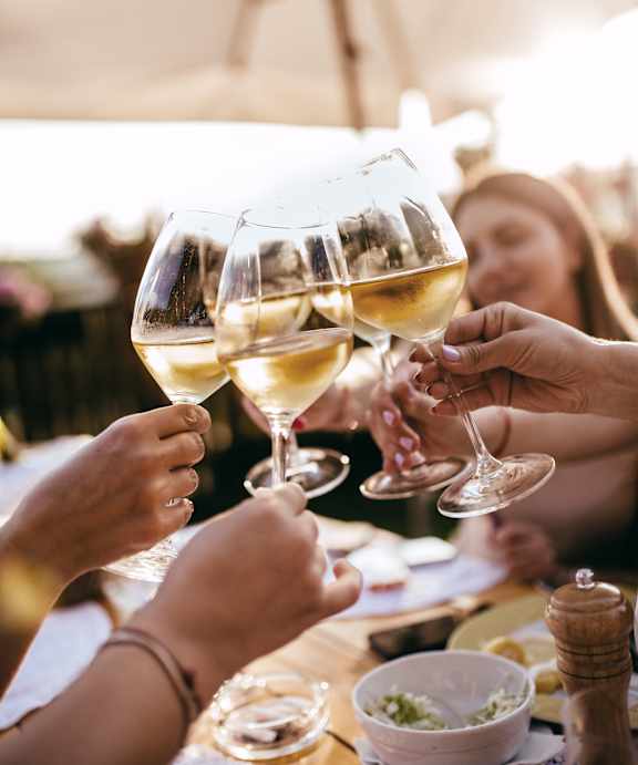 A group of people toasting with glasses of white wine at an outdoor table.