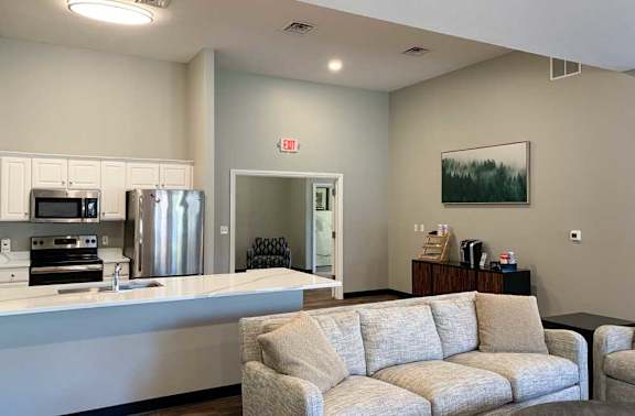 a modern kitchen with white cabinets and stainless steel appliances in a clubhosue with a coffee bar and grey couch