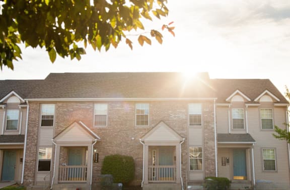 A row of houses with the sun shining through the trees.