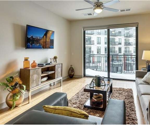 The living room with a couch, plush chairs, coffee table, decorations, a TV, and balcony at Inspire Apartments. 