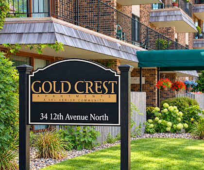 A sign for Gold Crest Apartments stands in front of a building.