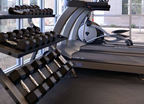 a treadmill and weights in a gym with a large window  at Epic Apartments, Denton, TX