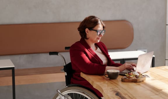 a woman in a wheelchair sitting at a table with a laptop