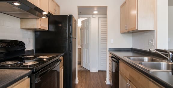 a kitchen with black appliances and wooden cabinets and a door to a hallway at Crawford Square Apartments