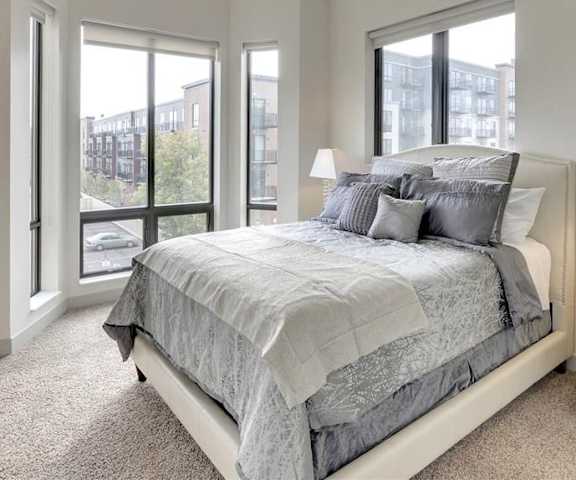 A bedroom with a queen-size bed, decorations, window, and nightstands at Inspire Apartments. 