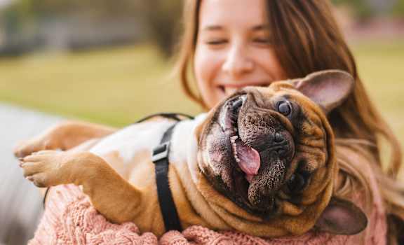 A woman is holding a happy dog in her arms.