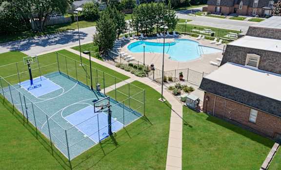 A basketball court is surrounded by a fence and a pool is in the background.