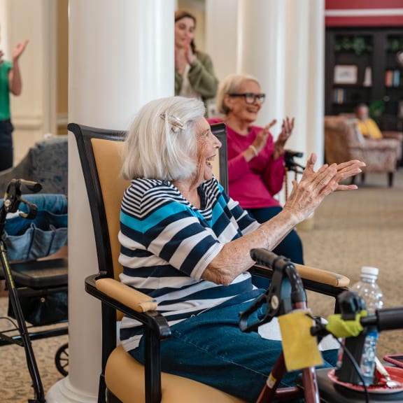 an older woman sitting in a chair in a lobby with her hands in the air
