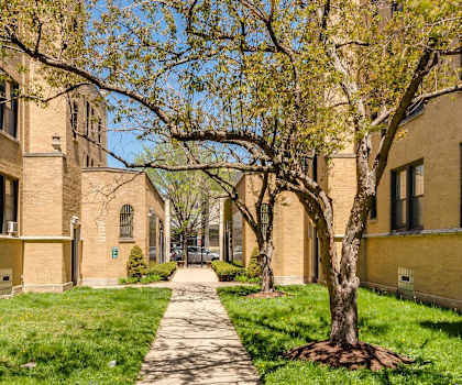 a sidewalk between two brick apartment buildings with grass and trees