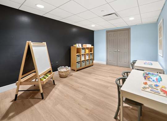 A room with a whiteboard, a table with art supplies, and a cabinet with shelves.