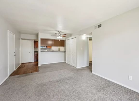 A spacious living room with a ceiling fan and carpeted floor.